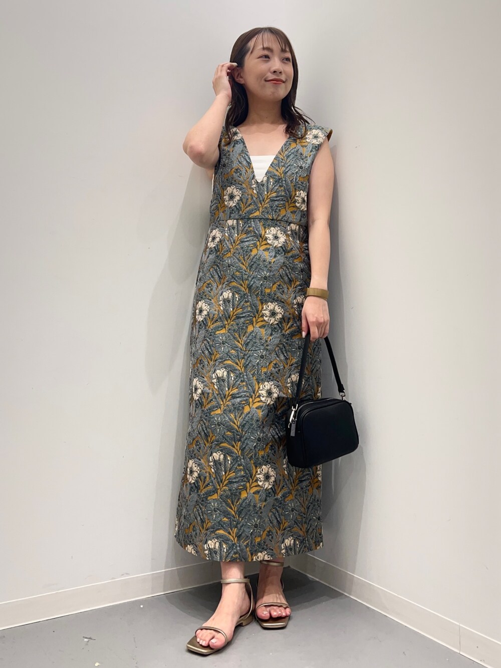 イエロー系のワンピース、ゴールド系のサンダル、ブラック系のショルダーバッグを着用したレディースの夏コーディネートの2枚目の写真