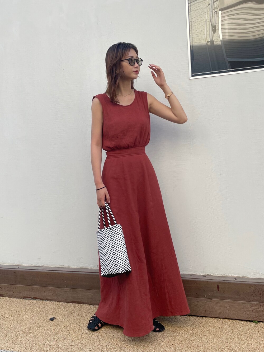 オレンジ系のワンピース、ブラック系のかごバッグ、ブラック系のサンダルを着用したレディースの夏コーディネートの2枚目の写真