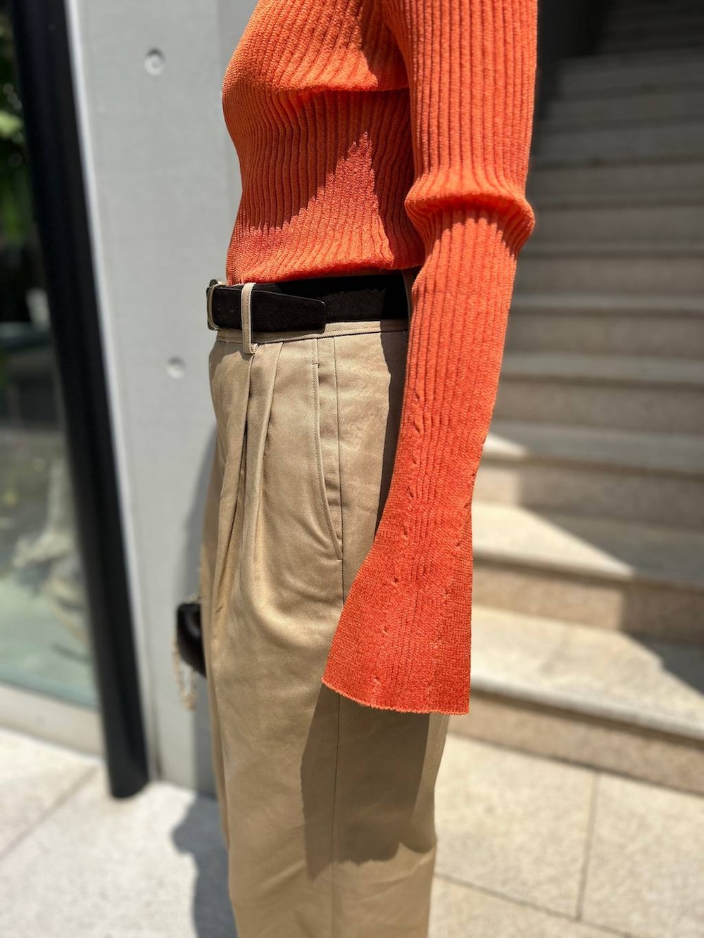 ベージュ系のチノパンツ、オレンジ系のニット/セーター、ブラウン系のベルトを着用したレディースの夏コーディネートの5枚目の写真