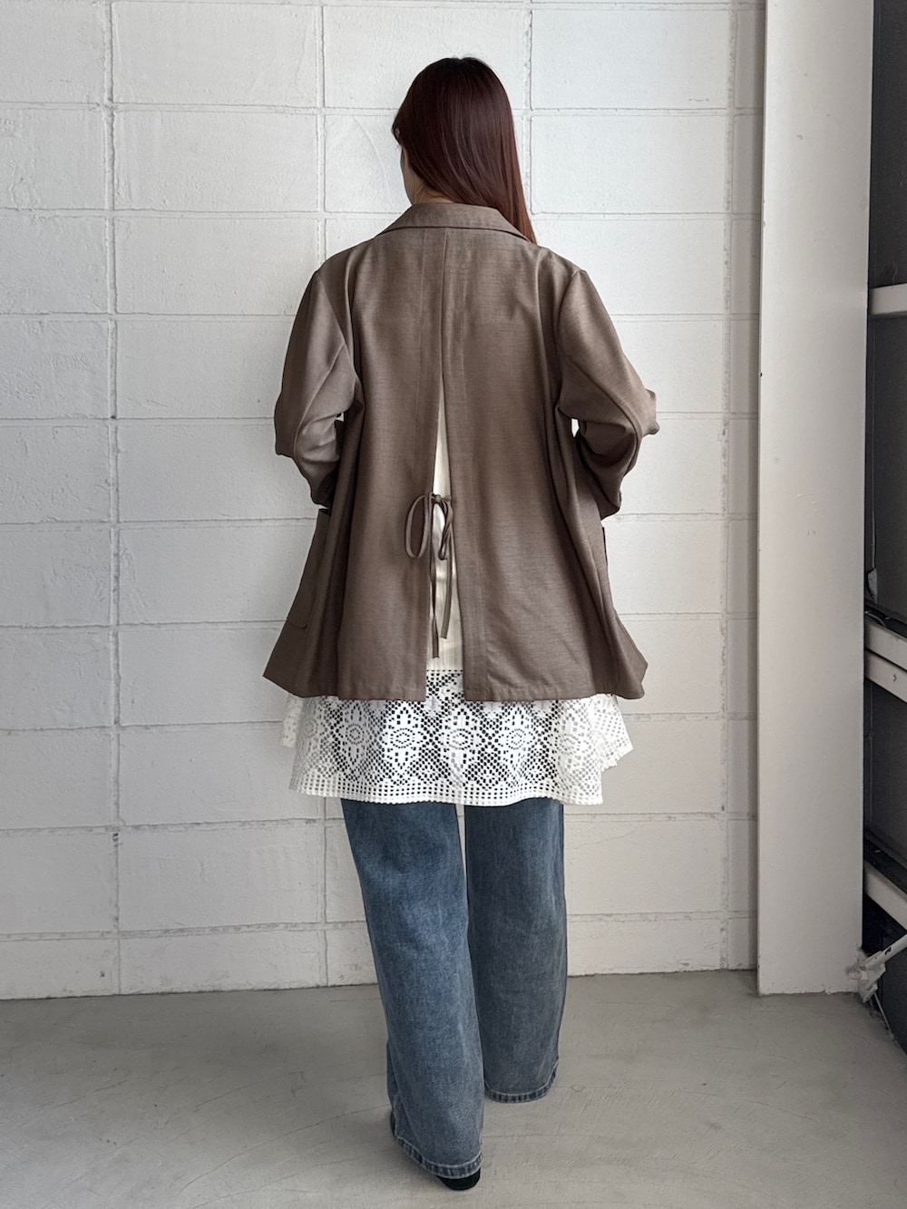 ブラウン系のテーラードジャケット、ホワイト系のワンピース、ブラック系のデニムパンツを着用したレディースの秋コーディネートの2枚目の写真