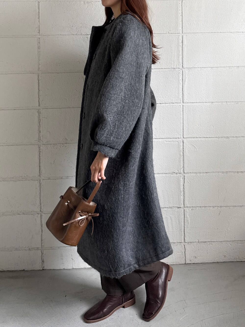 ブラウン系のショルダーバッグ、ブラウン系のスラックス、グレー系のノーカラーコートを着用したレディースの冬コーディネートの3枚目の写真