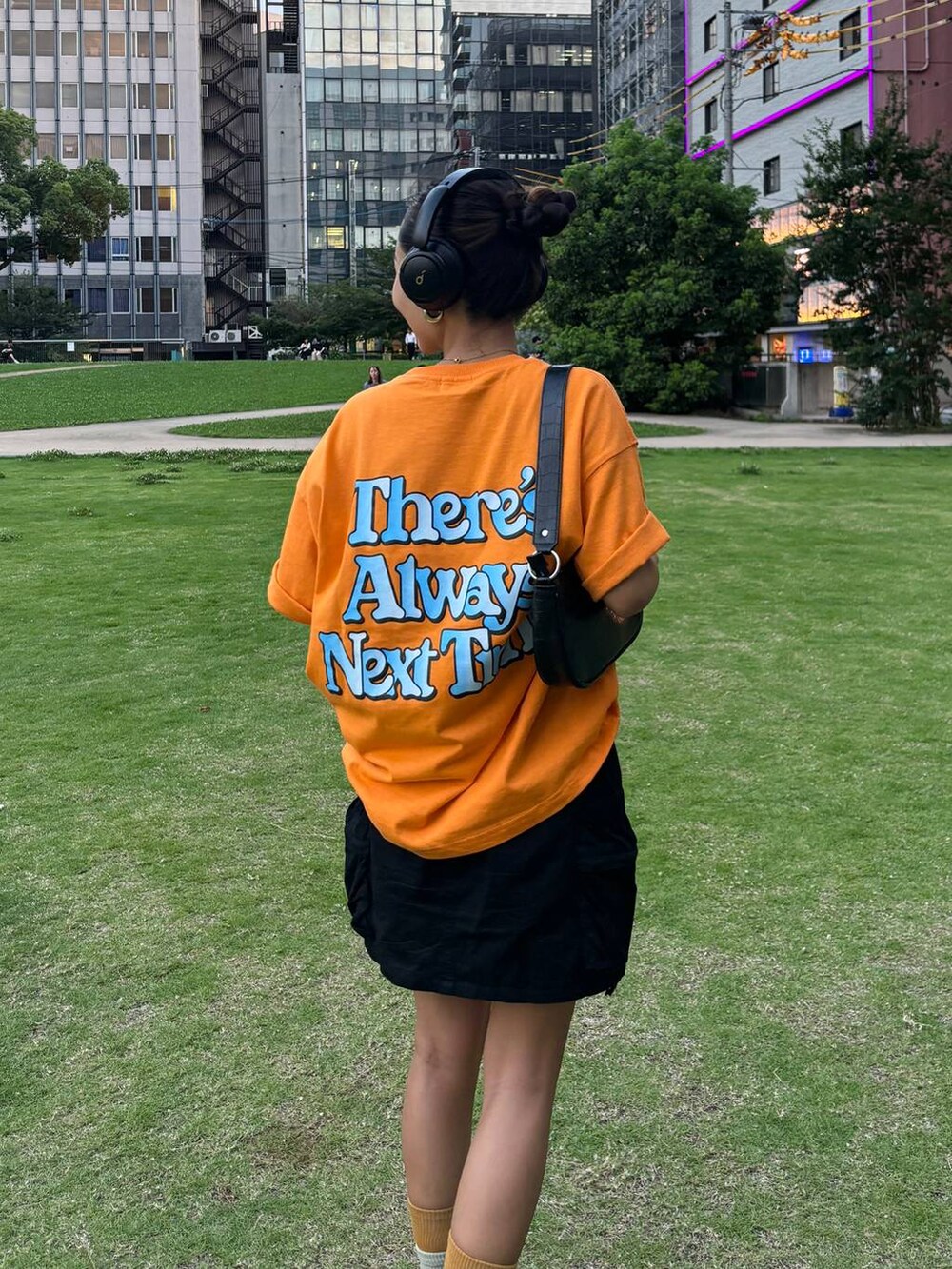 ブラック系のスニーカー、ブラック系のスカート、オレンジ系のTシャツ/カットソーを着用したレディースの夏コーディネートの3枚目の写真