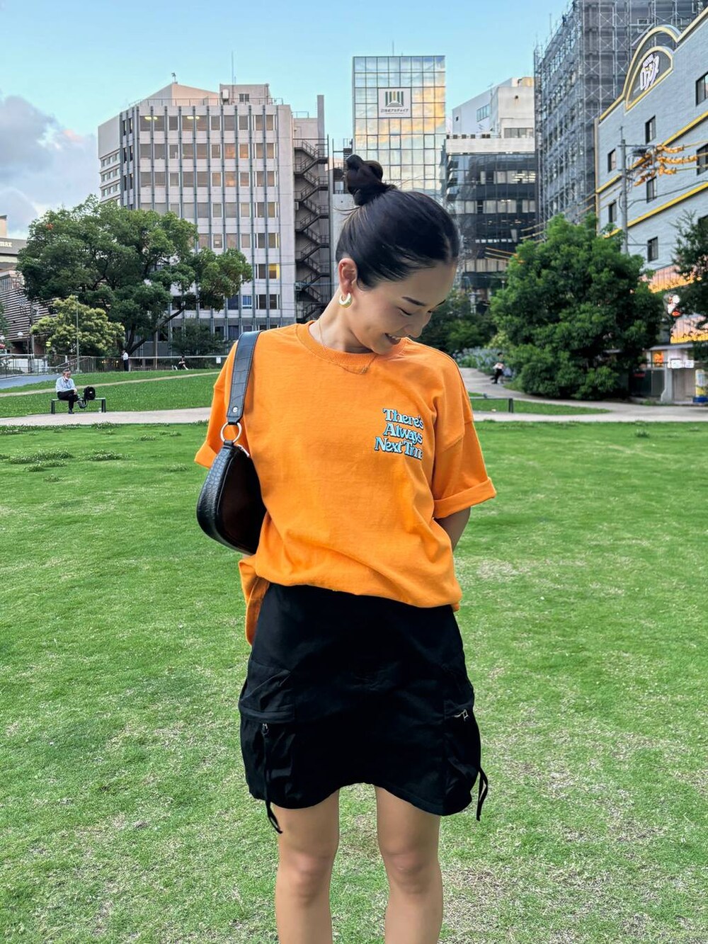 ブラック系のスニーカー、ブラック系のスカート、オレンジ系のTシャツ/カットソーを着用したレディースの夏コーディネートの4枚目の写真