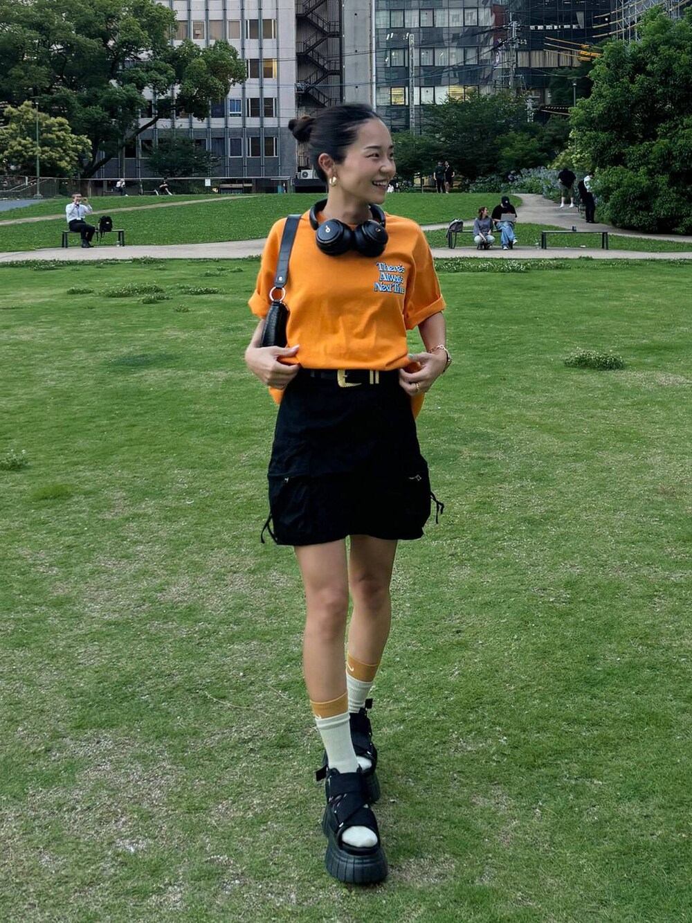 ブラック系のスニーカー、ブラック系のスカート、オレンジ系のTシャツ/カットソーを着用したレディースの夏コーディネートの2枚目の写真
