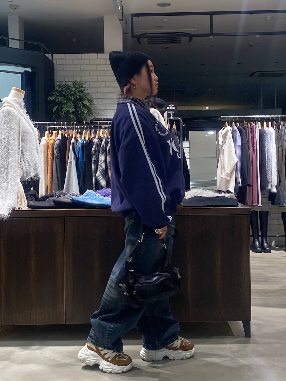 ベージュ系のスニーカー、ブラック系のショルダーバッグ、ブルー系のデニムパンツを着用したレディースの秋コーディネートの2枚目の写真