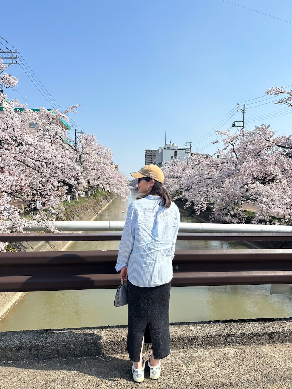 ブルー系のシャツ/ブラウス、グレー系のショルダーバッグ、ブラック系のスカートを着用したレディースの春コーディネートの2枚目の写真