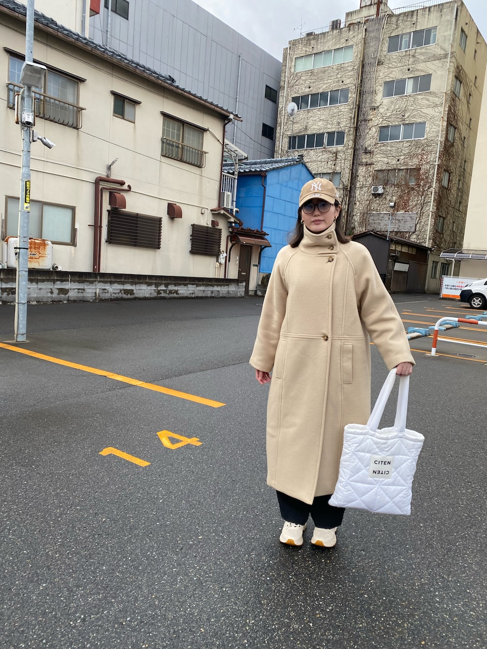 ホワイト系のトートバッグ、ベージュ系のチェスターコートを着用したレディースの冬コーディネートの2枚目の写真