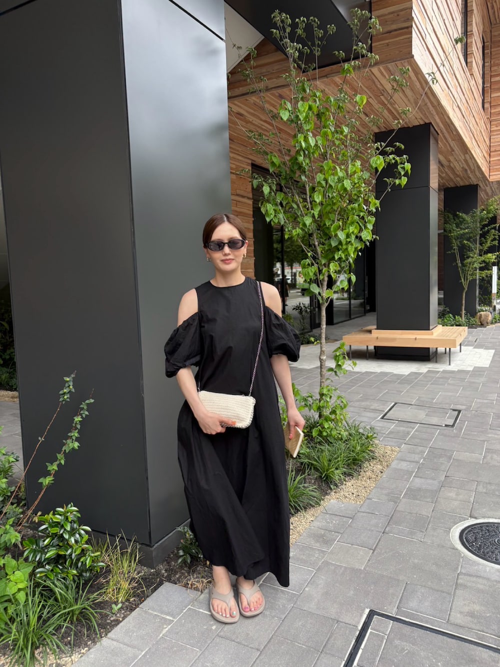 ブラック系のワンピース、ベージュ系のサンダル、ベージュ系のバッグを着用したレディースの夏コーディネートの2枚目の写真
