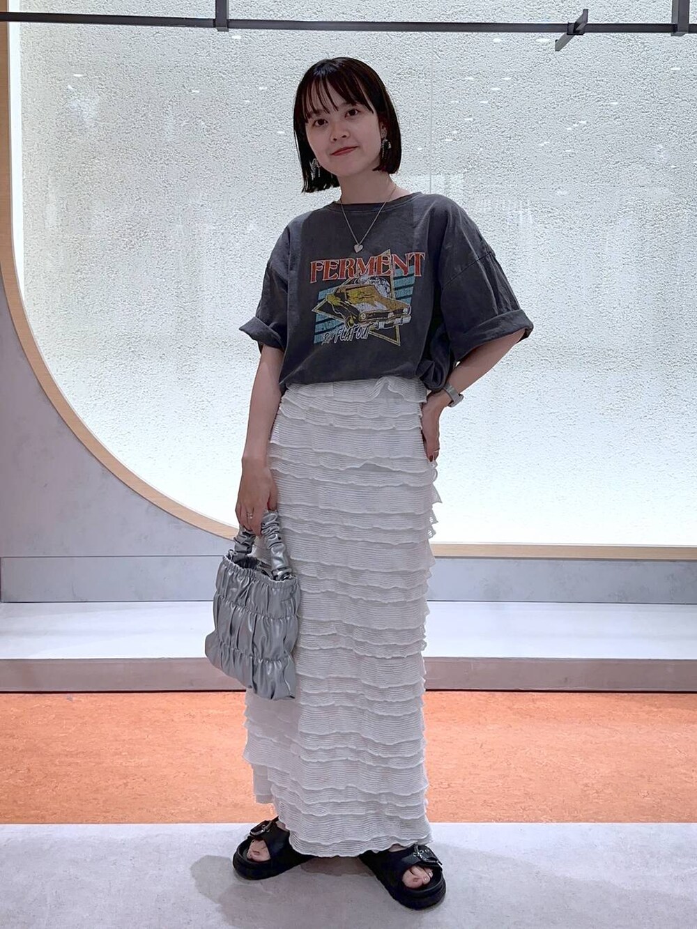 ホワイト系のスカート、グレー系のショルダーバッグ、グレー系のTシャツ/カットソーを着用したレディースの夏コーディネートの2枚目の写真