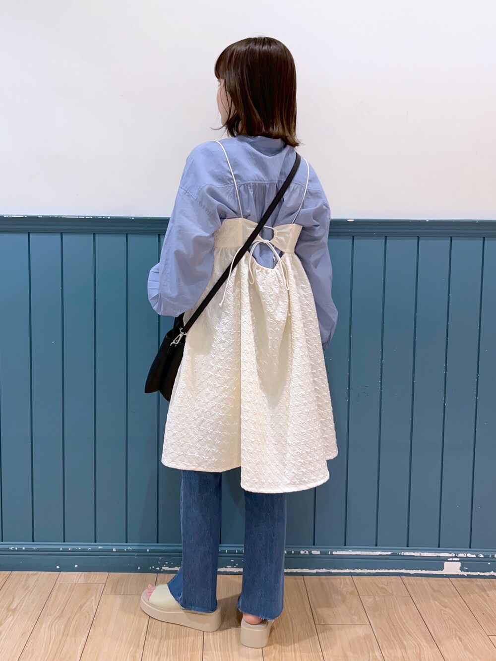 ブラック系のショルダーバッグ、ホワイト系のチュニック、ブルー系のデニムパンツを着用したレディースの春コーディネートの2枚目の写真