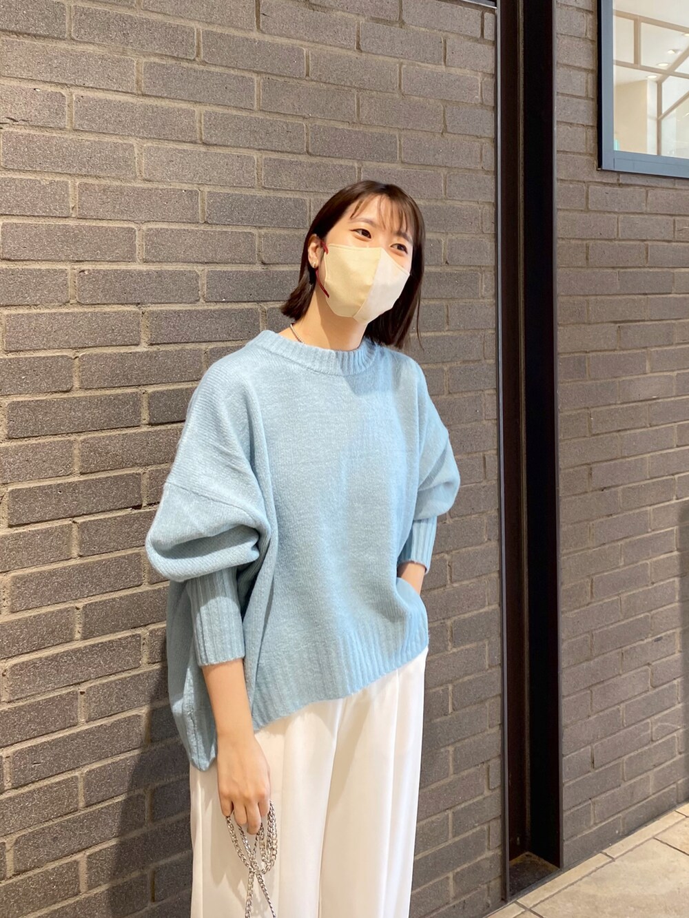 ブルー系のニット/セーター、ホワイト系のスラックス、ブラック系のショルダーバッグを着用したレディースの秋コーディネートの2枚目の写真