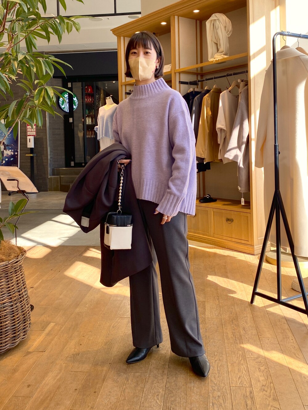 グレー系のノーカラーコート、パープル系のニット/セーター、グレー系のスラックスを着用したレディースの冬コーディネートの2枚目の写真