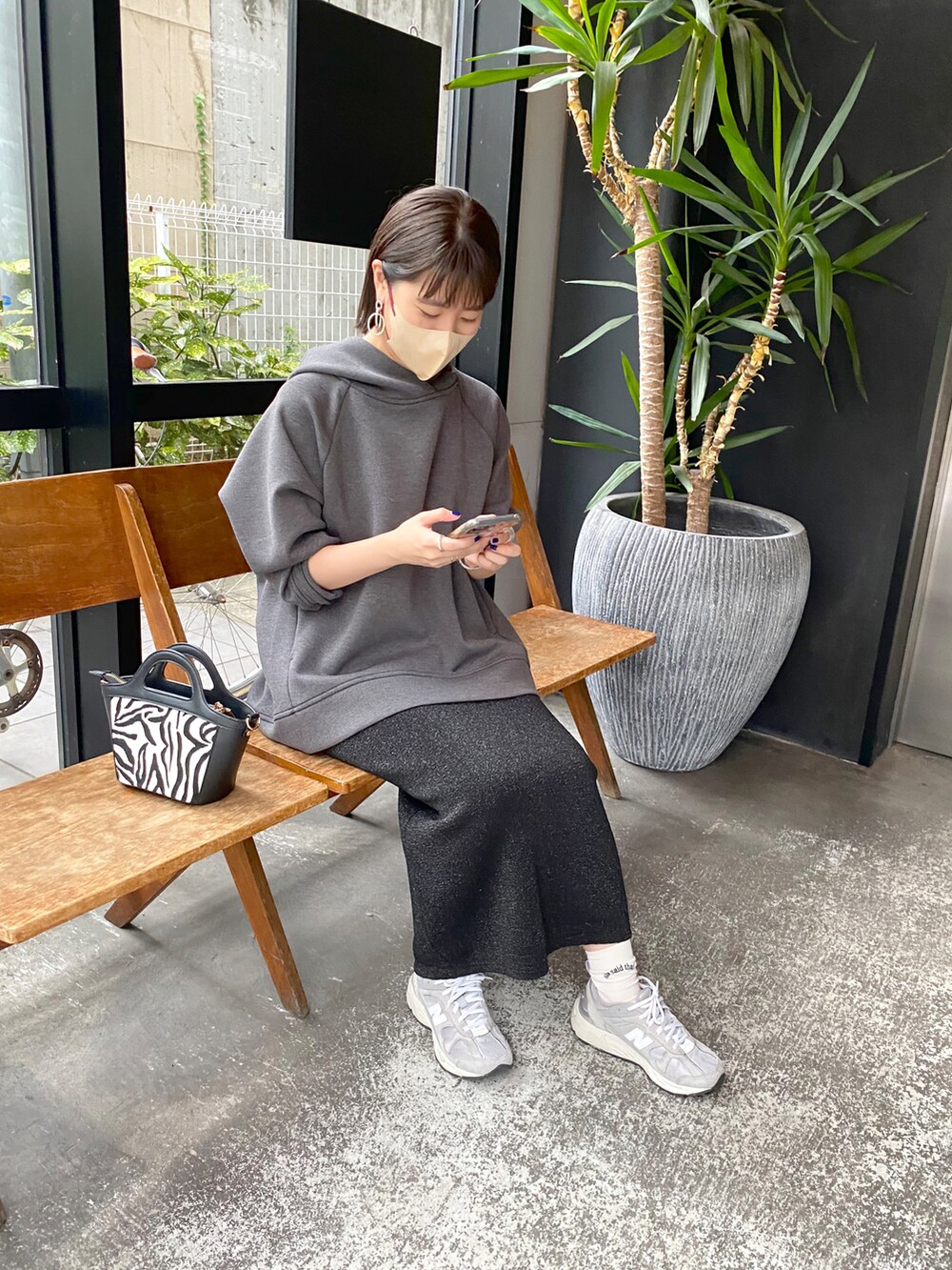 グレー系のパーカー、ブラック系のスカート、ブラック系のショルダーバッグを着用したレディースの秋コーディネートの2枚目の写真