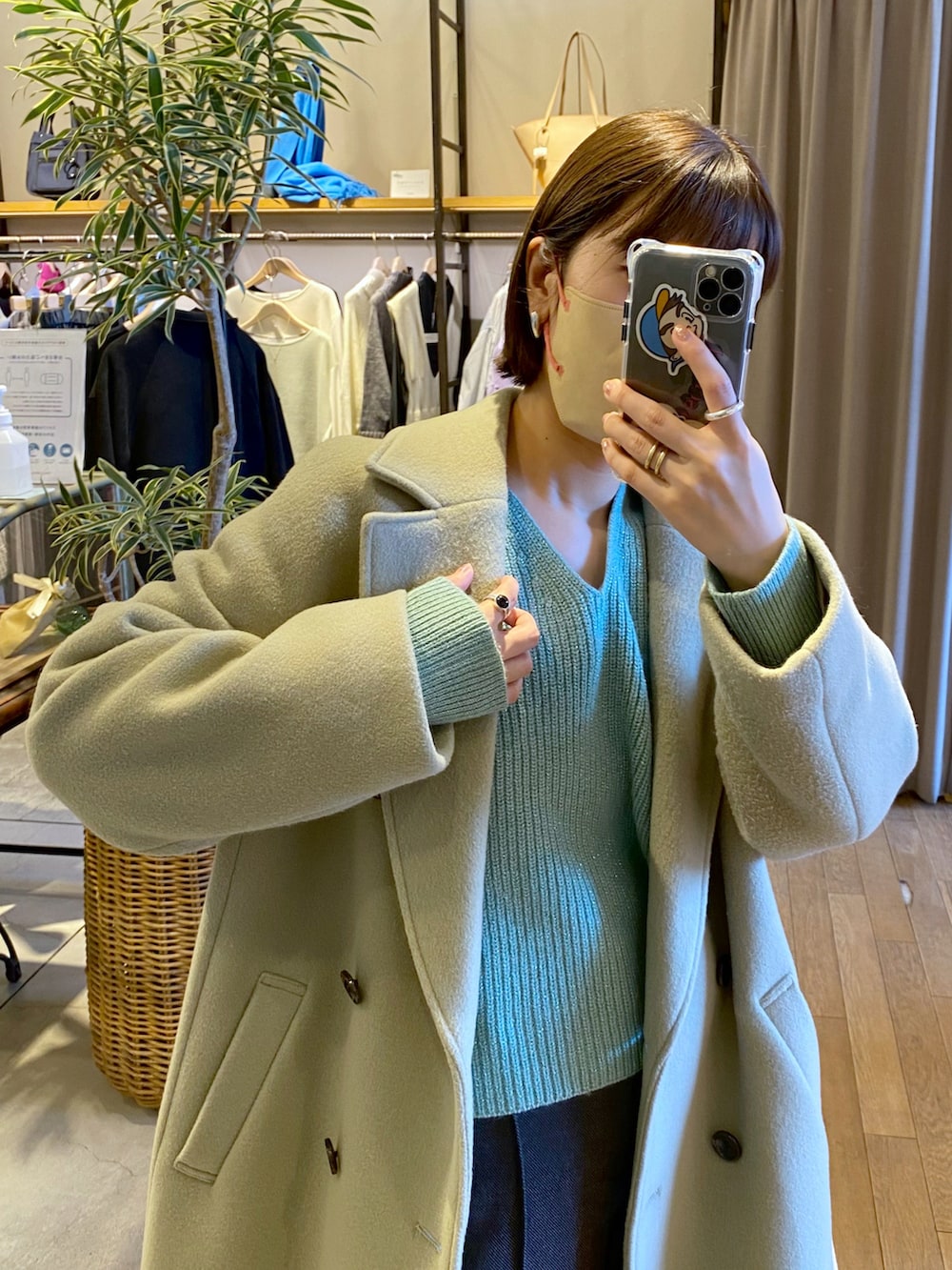 グリーン系のチェスターコート、グリーン系のニット/セーター、ブラック系のトートバッグを着用したレディースの冬コーディネートの2枚目の写真