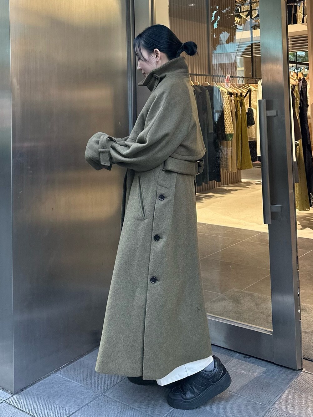 グリーン系のステンカラーコートを着用したレディースの秋コーディネートの2枚目の写真