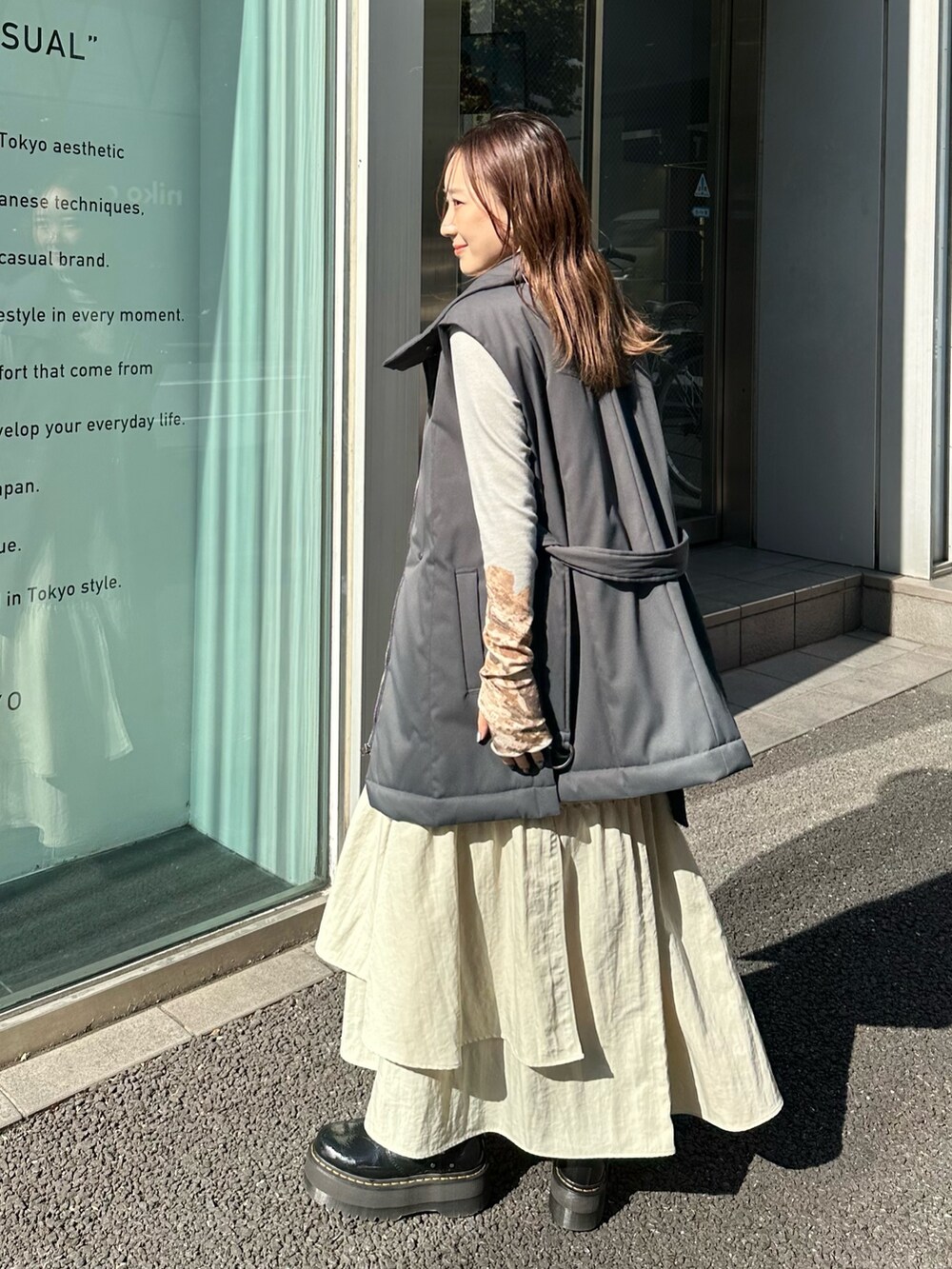 ベージュ系のスカート、ブラック系のダウンベスト、ブルー系のTシャツ/カットソーを着用したレディースの秋コーディネートの2枚目の写真