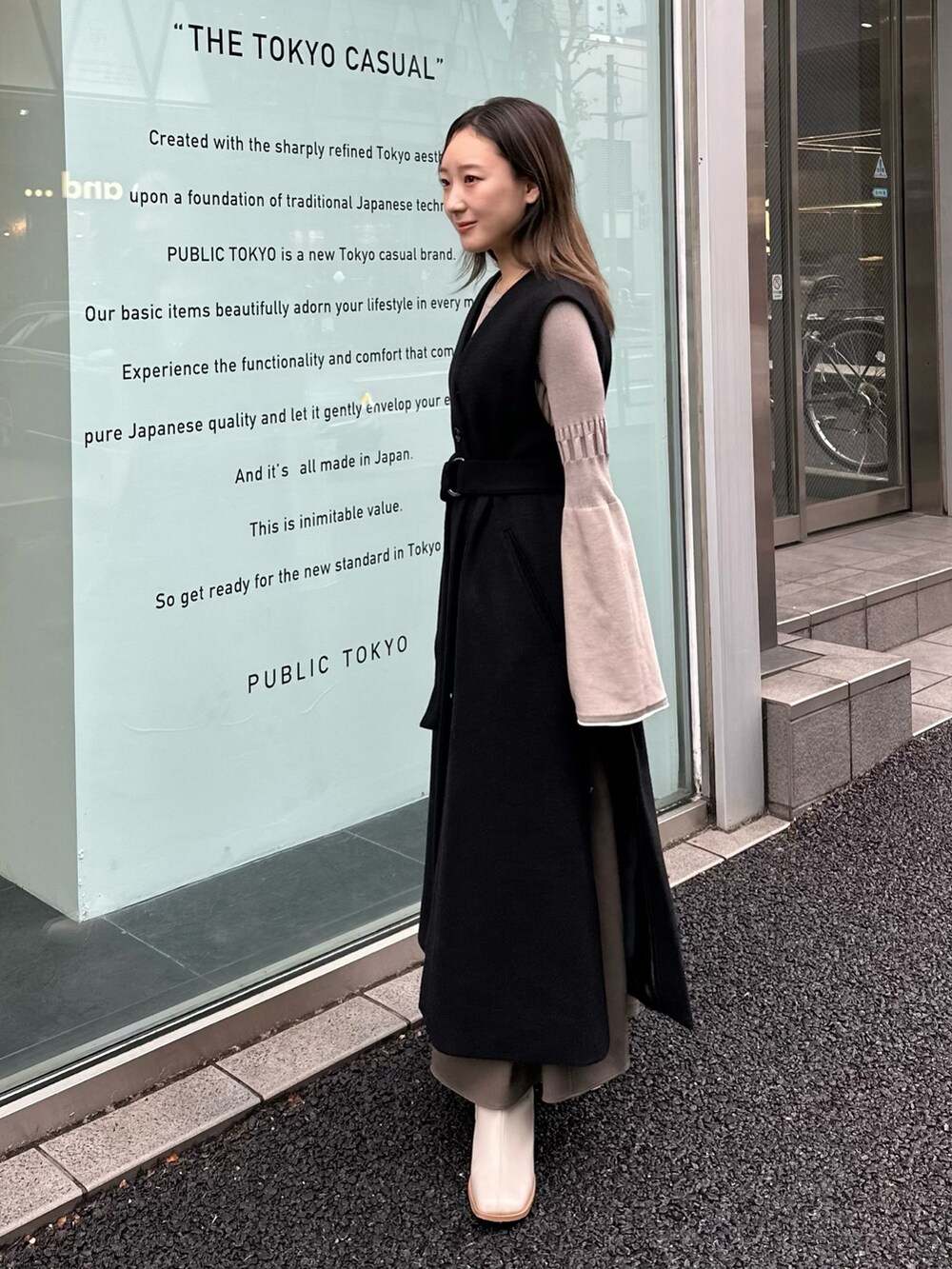 グレー系のワンピース、ブラック系のステンカラーコートを着用したレディースの秋コーディネートの2枚目の写真