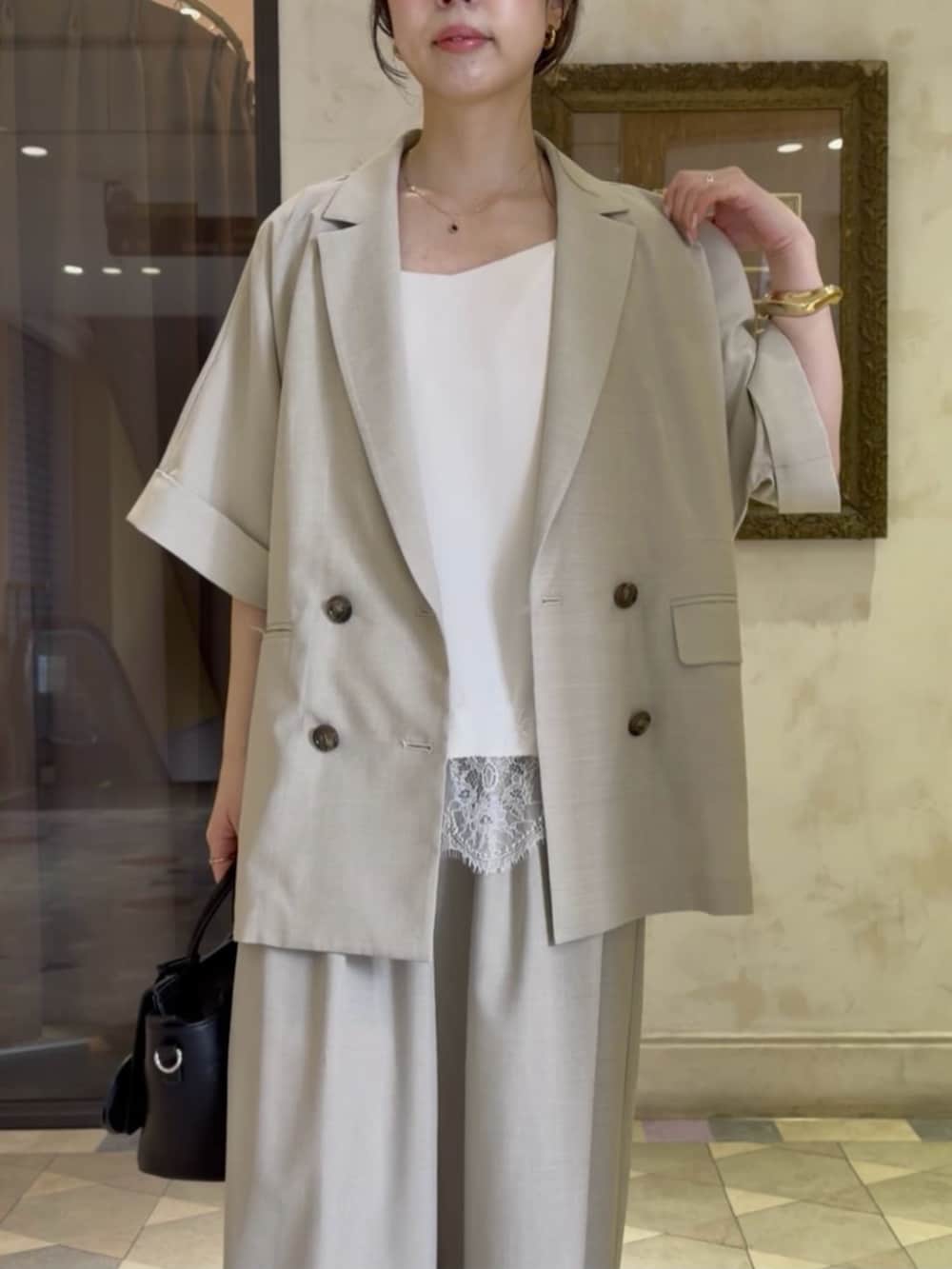 ブラック系のハンドバッグ、ベージュ系のテーラードジャケット、ホワイト系のキャミソールを着用したレディースの春コーディネートの5枚目の写真