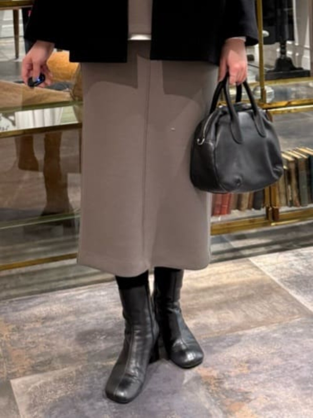 ブラウン系のスカート、ブラック系のノーカラーコートを着用したレディースの冬コーディネートの4枚目の写真