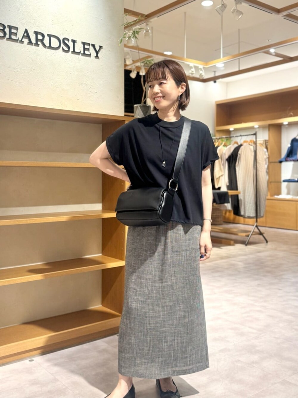 ブラック系のショルダーバッグ、ベージュ系のスカート、ゴールド系のネックレスを着用したレディースの春コーディネートの9枚目の写真