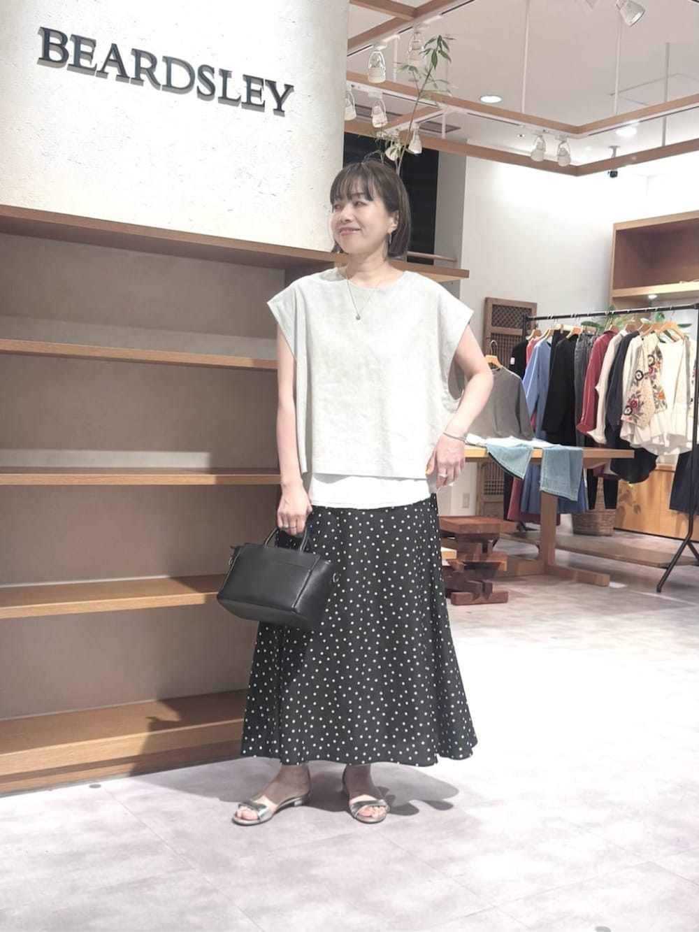 ブラック系のハンドバッグ、ブラック系のスカート、ベージュ系のシャツ/ブラウスを着用したレディースの春コーディネートの2枚目の写真