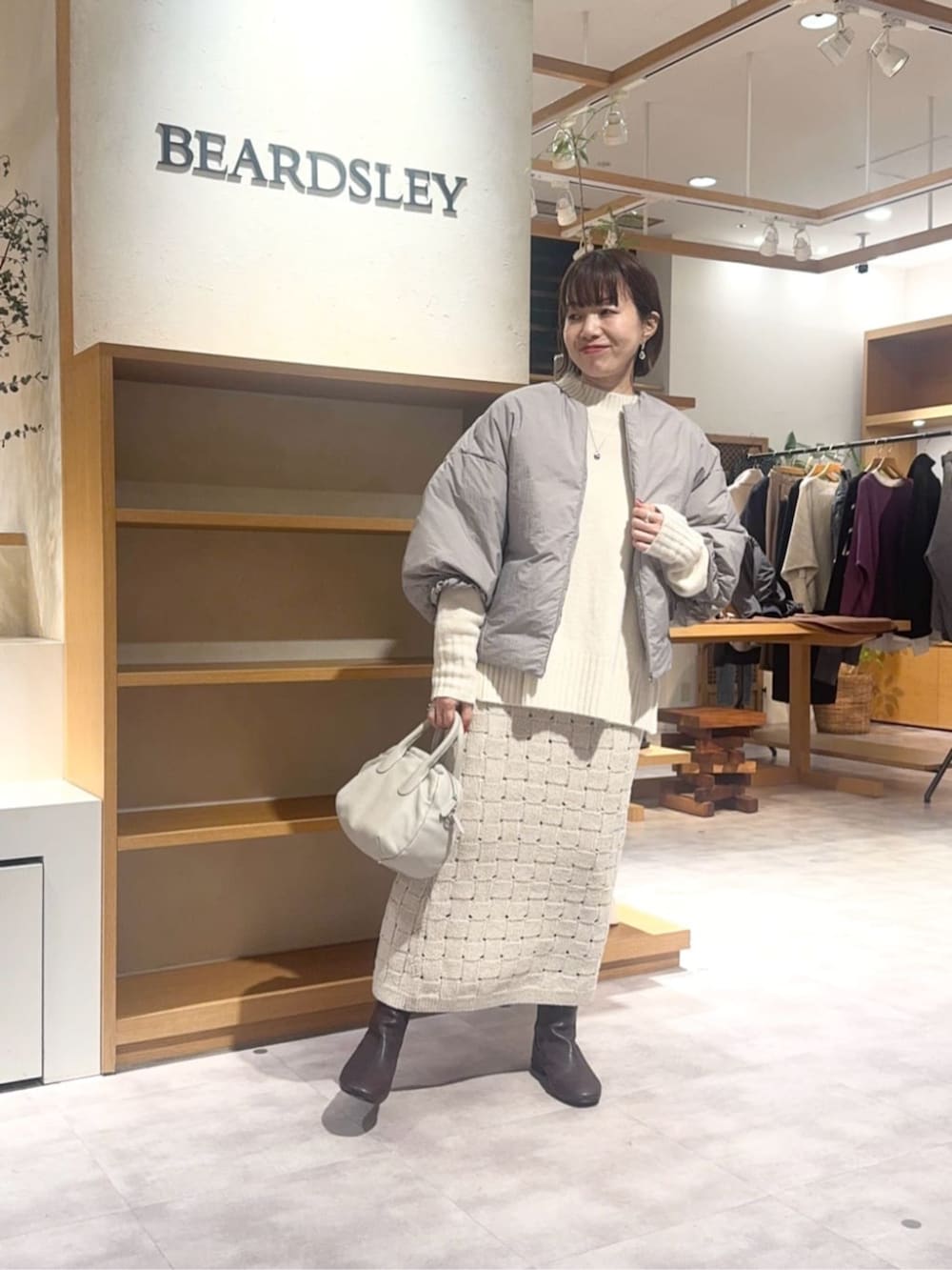 グレー系のボストンバッグ、ベージュ系のスカート、ブラウン系のダウンジャケット/コートを着用したレディースの冬コーディネートの2枚目の写真