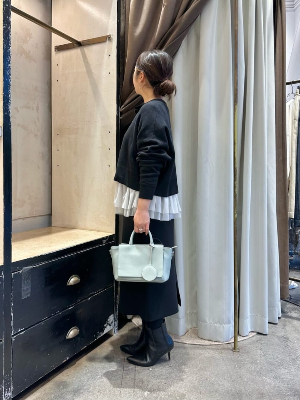 グリーン系のハンドバッグ、ブラック系のスカート、ブラック系のブーツを着用したレディースの冬コーディネートの3枚目の写真