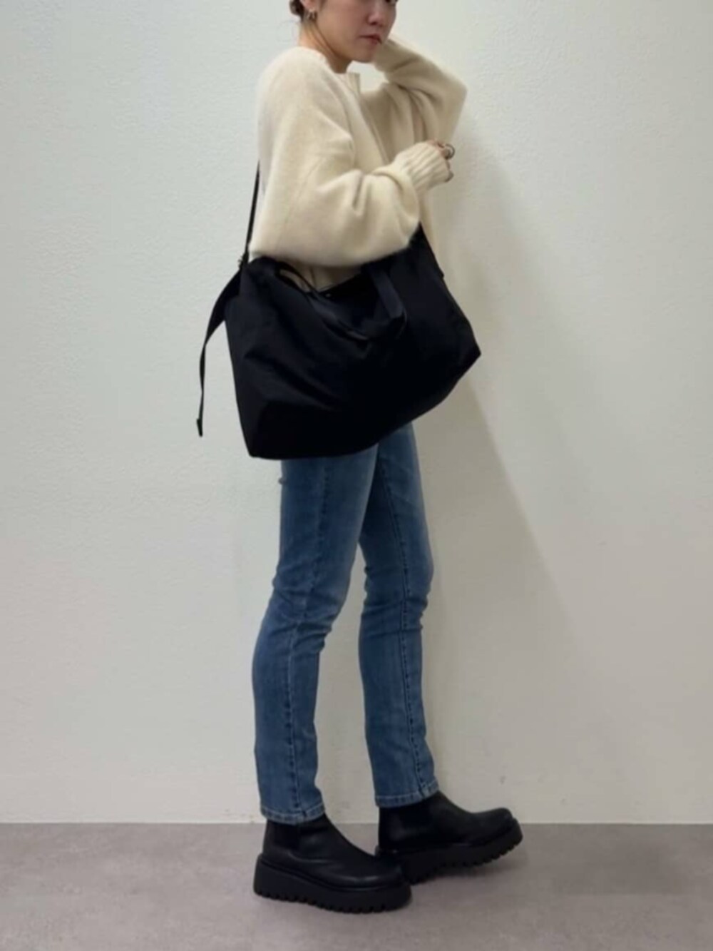 ブルー系のデニムパンツ、ブラック系のトートバッグ、ホワイト系のニット/セーターを着用したレディースの秋コーディネートの2枚目の写真