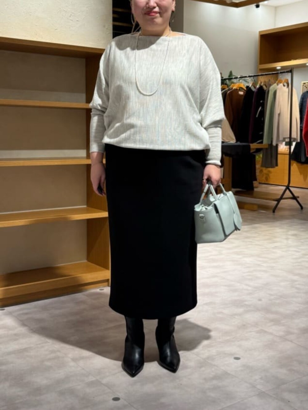 グリーン系のハンドバッグ、グレー系のニット/セーター、ブラック系のブーツを着用したレディースの冬コーディネートの4枚目の写真