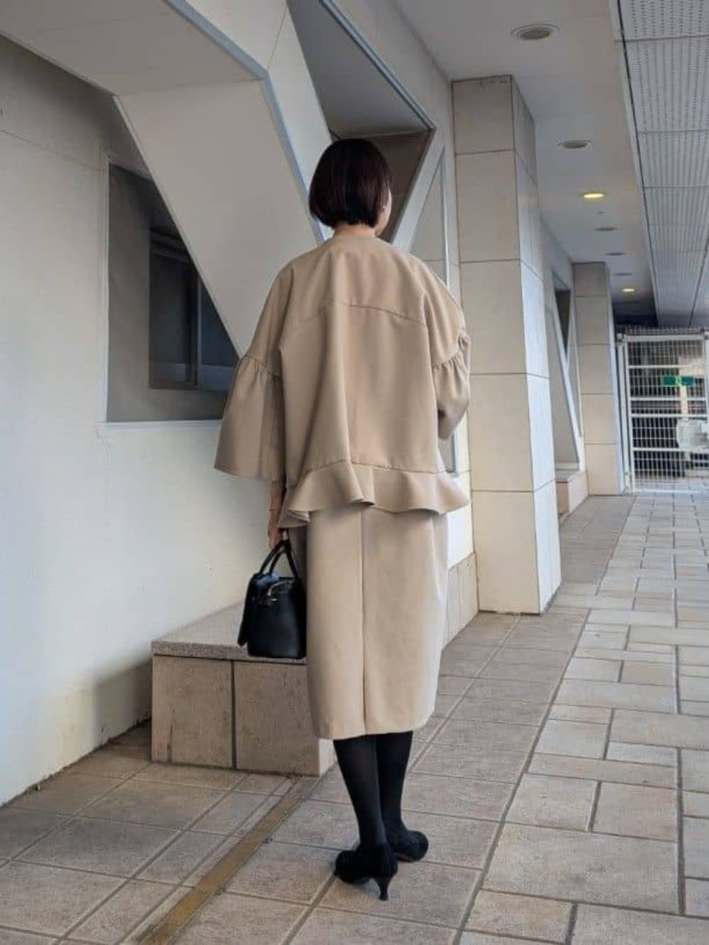 ブラック系のハンドバッグ、ベージュ系のワンピース、ベージュ系のその他アウターを着用したレディースの冬コーディネートの4枚目の写真