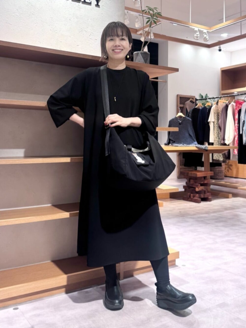 ブラック系のワンピース、ブラック系のトートバッグ、ホワイト系のポーチを着用したレディースの秋コーディネートの3枚目の写真