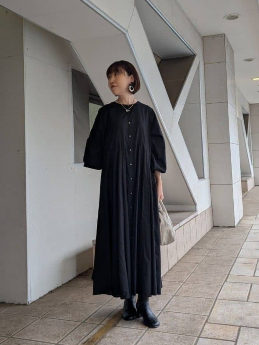 ベージュ系のショルダーバッグ、ブラック系のベスト、ブラック系のワンピースを着用したレディースの冬コーディネートの5枚目の写真