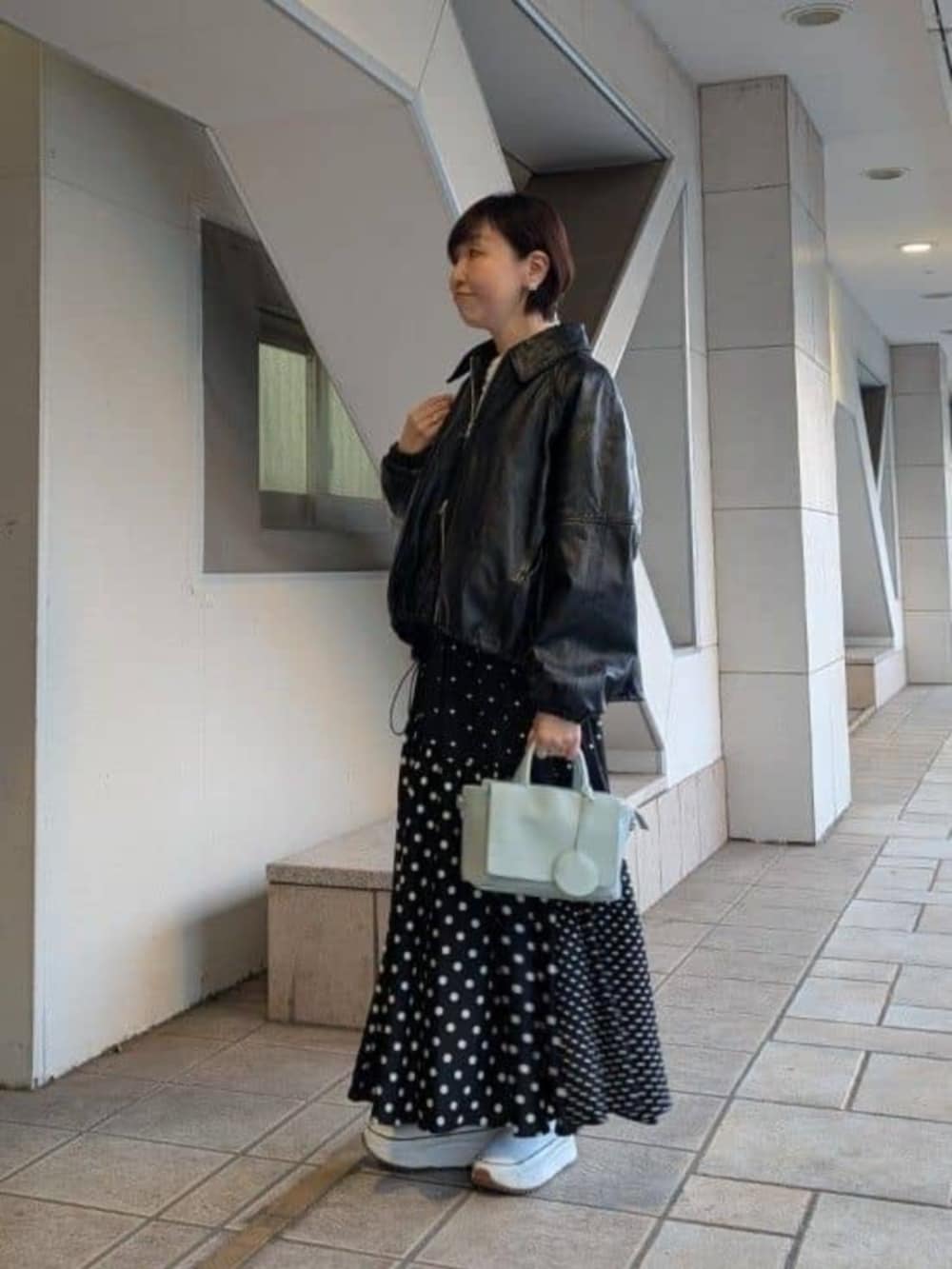 グリーン系のハンドバッグ、ブラック系のスカート、ブラック系のブルゾンを着用したレディースの冬コーディネートの2枚目の写真