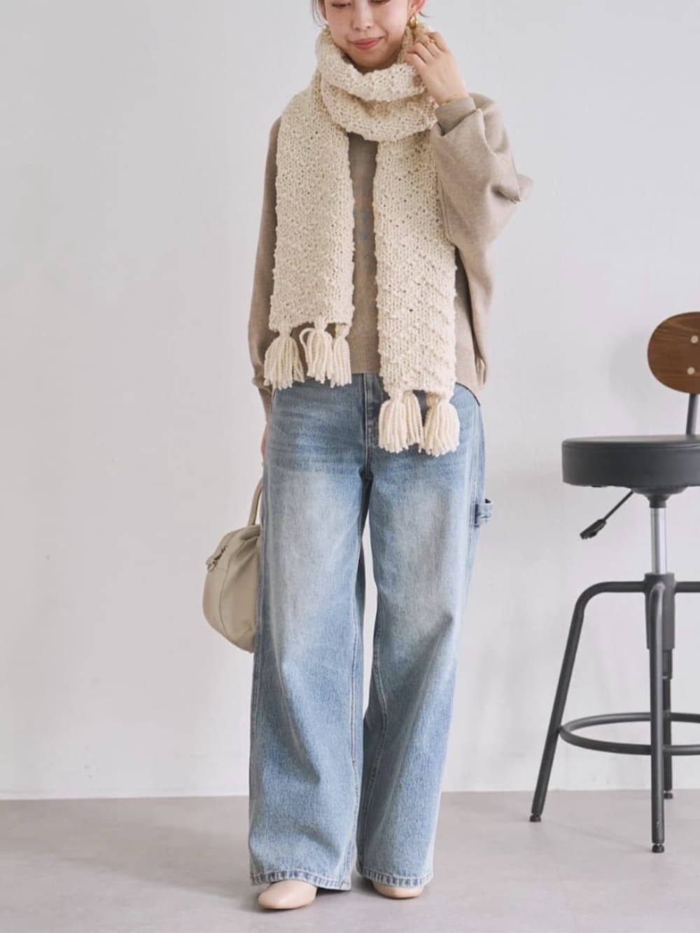 ブルー系のデニムパンツ、ブラウン系のニット/セーター、ホワイト系のマフラーを着用したレディースの秋コーディネートの2枚目の写真