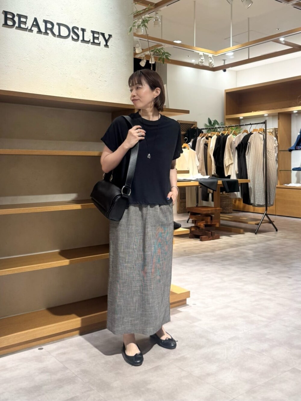 ブラック系のショルダーバッグ、ベージュ系のスカート、ゴールド系のネックレスを着用したレディースの春コーディネートの7枚目の写真