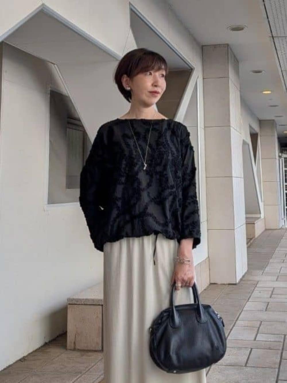 ブラック系のトートバッグ、ブラック系のその他アウター、ベージュ系のスカートを着用したレディースの夏コーディネートの6枚目の写真