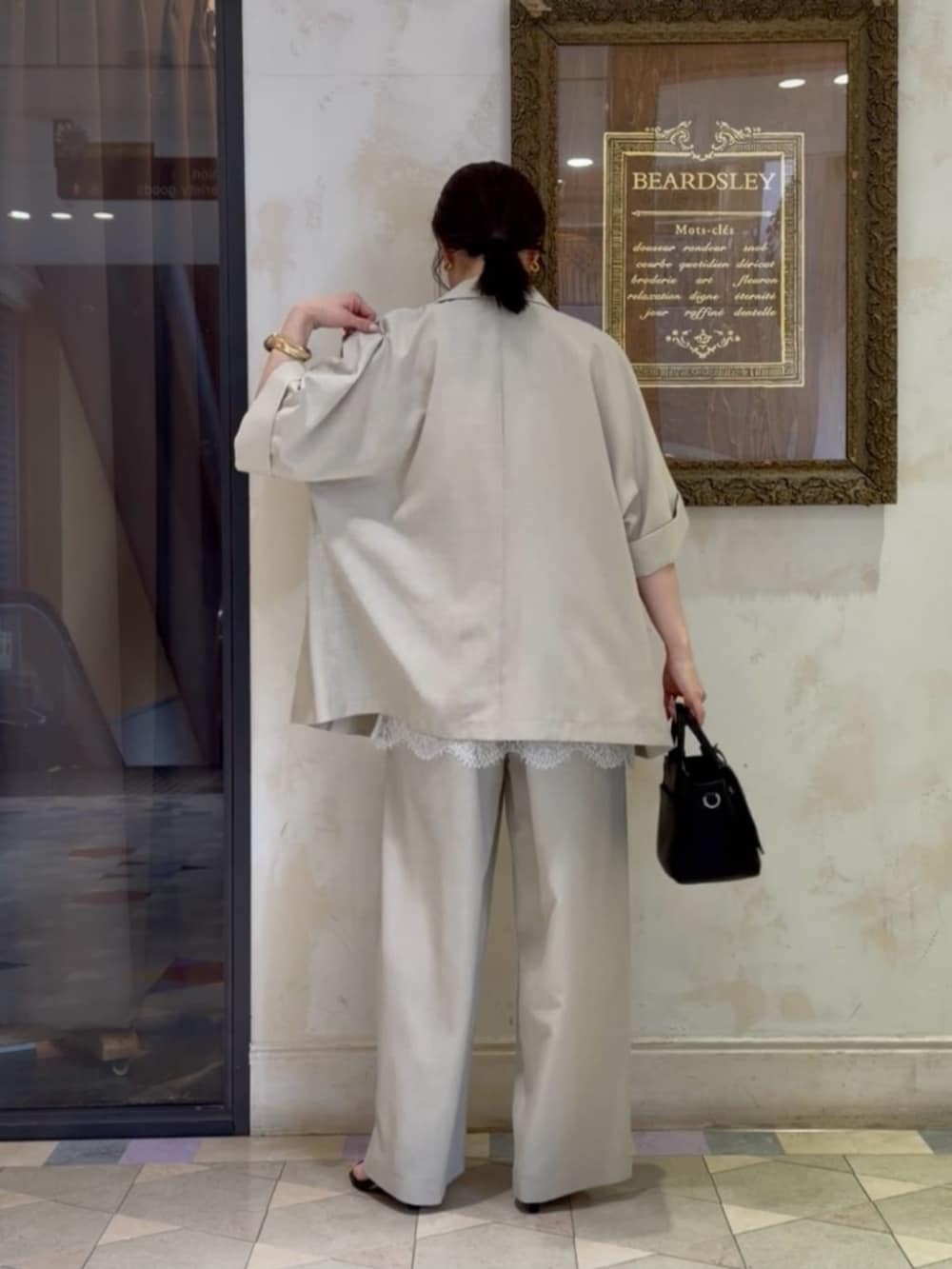 ブラック系のハンドバッグ、ベージュ系のテーラードジャケット、ホワイト系のキャミソールを着用したレディースの春コーディネートの3枚目の写真