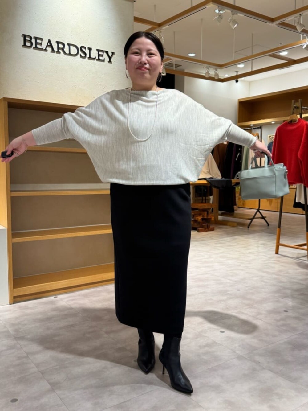 グリーン系のハンドバッグ、グレー系のニット/セーター、ブラック系のブーツを着用したレディースの冬コーディネートの6枚目の写真