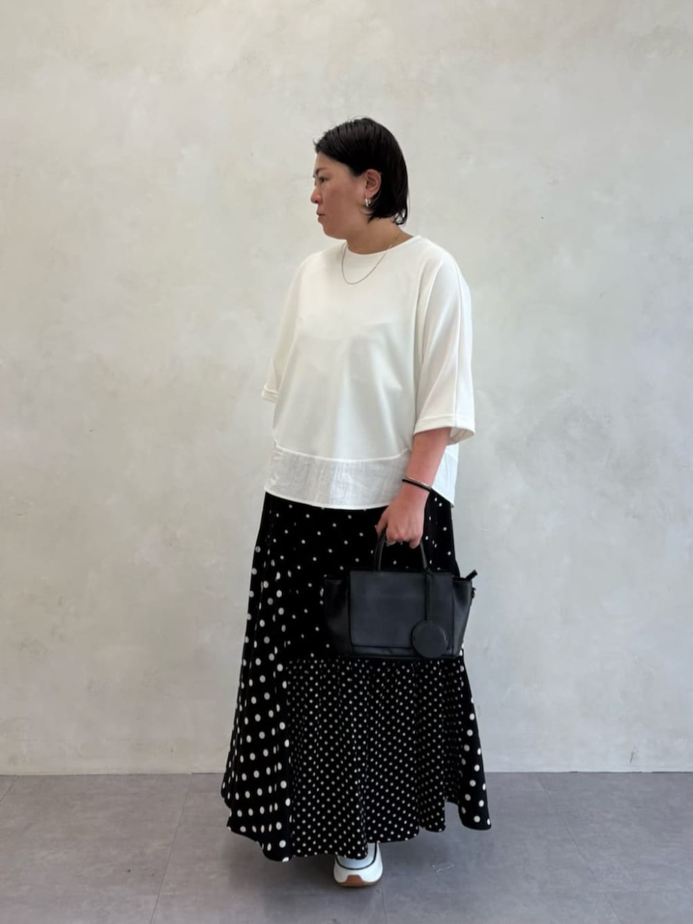 ブラック系のスカート、ホワイト系のTシャツ/カットソー、ホワイト系のスニーカーを着用したレディースの春コーディネートの2枚目の写真