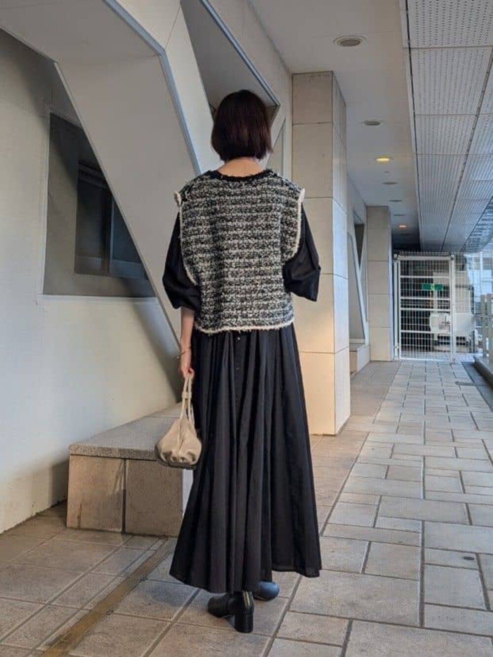 ベージュ系のショルダーバッグ、ブラック系のベスト、ブラック系のワンピースを着用したレディースの冬コーディネートの3枚目の写真