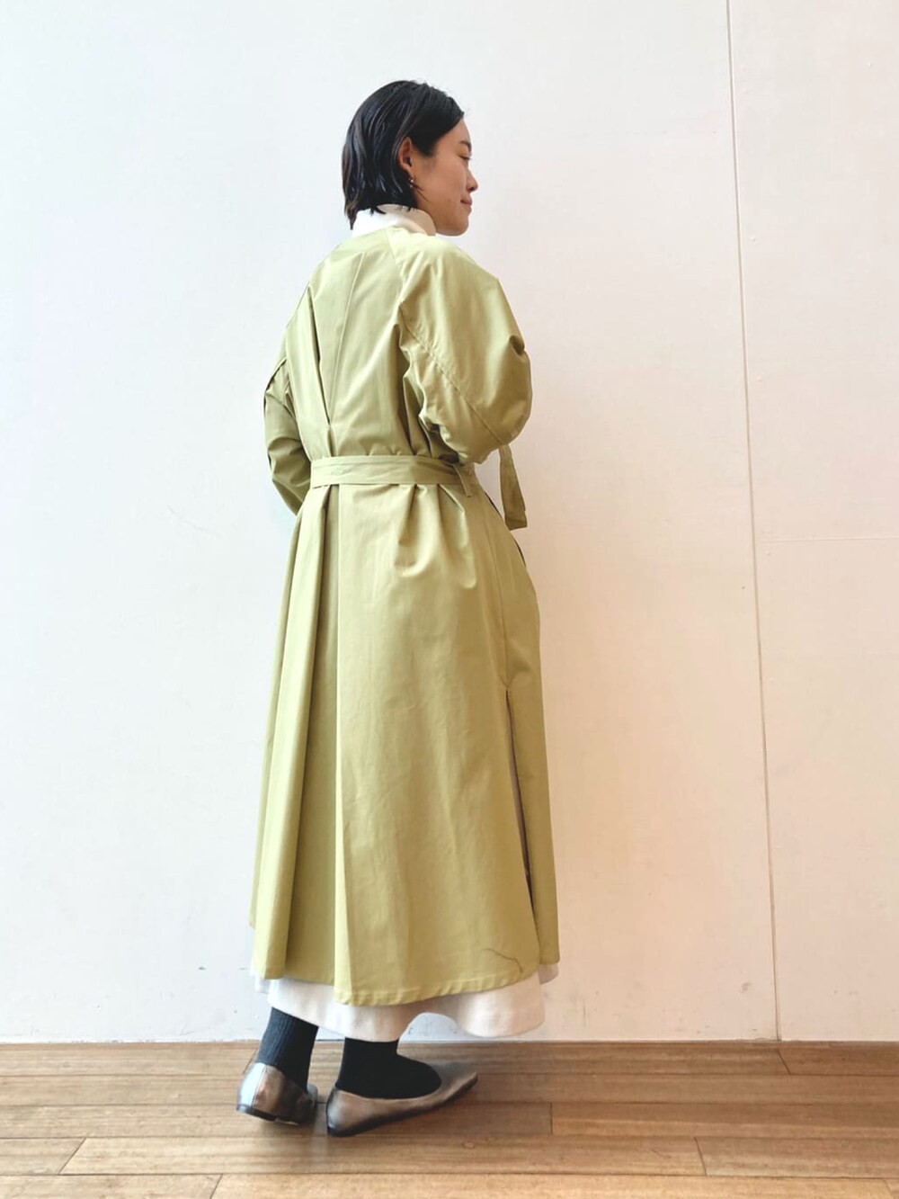 グリーン系のトレンチコート、ホワイト系のニット/セーター、グレー系のワンピースを着用したレディースの冬コーディネートの2枚目の写真