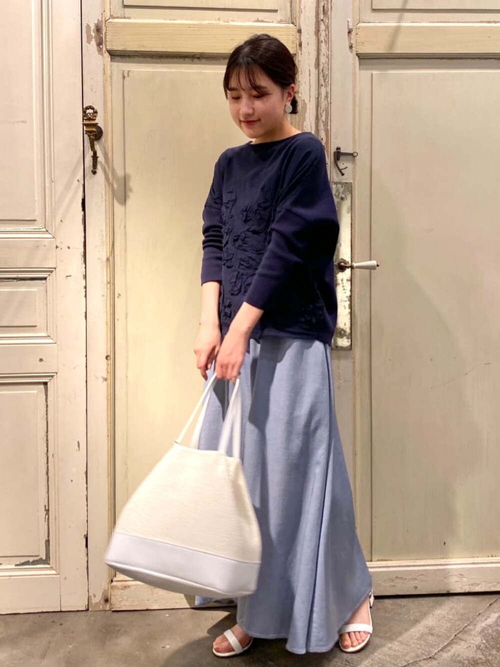ブルー系のニット/セーター、ホワイト系のトートバッグ、ブルー系のスカートを着用したレディースの春コーディネートの3枚目の写真