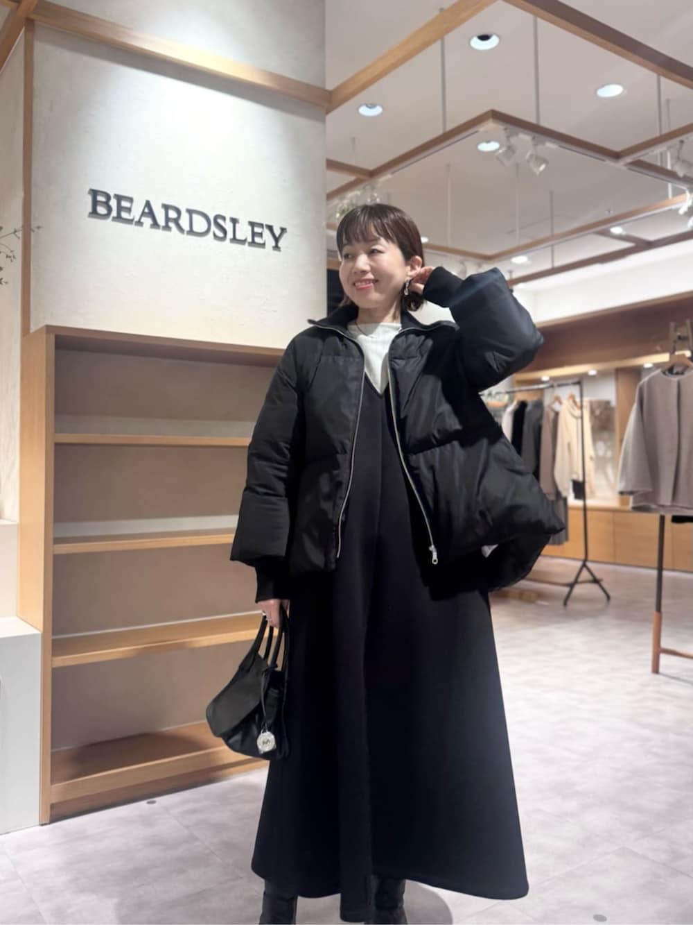 ブラック系のトートバッグ、ブラック系のジャンパースカート、ブラック系のダウンジャケット/コートを着用したレディースの冬コーディネートの2枚目の写真