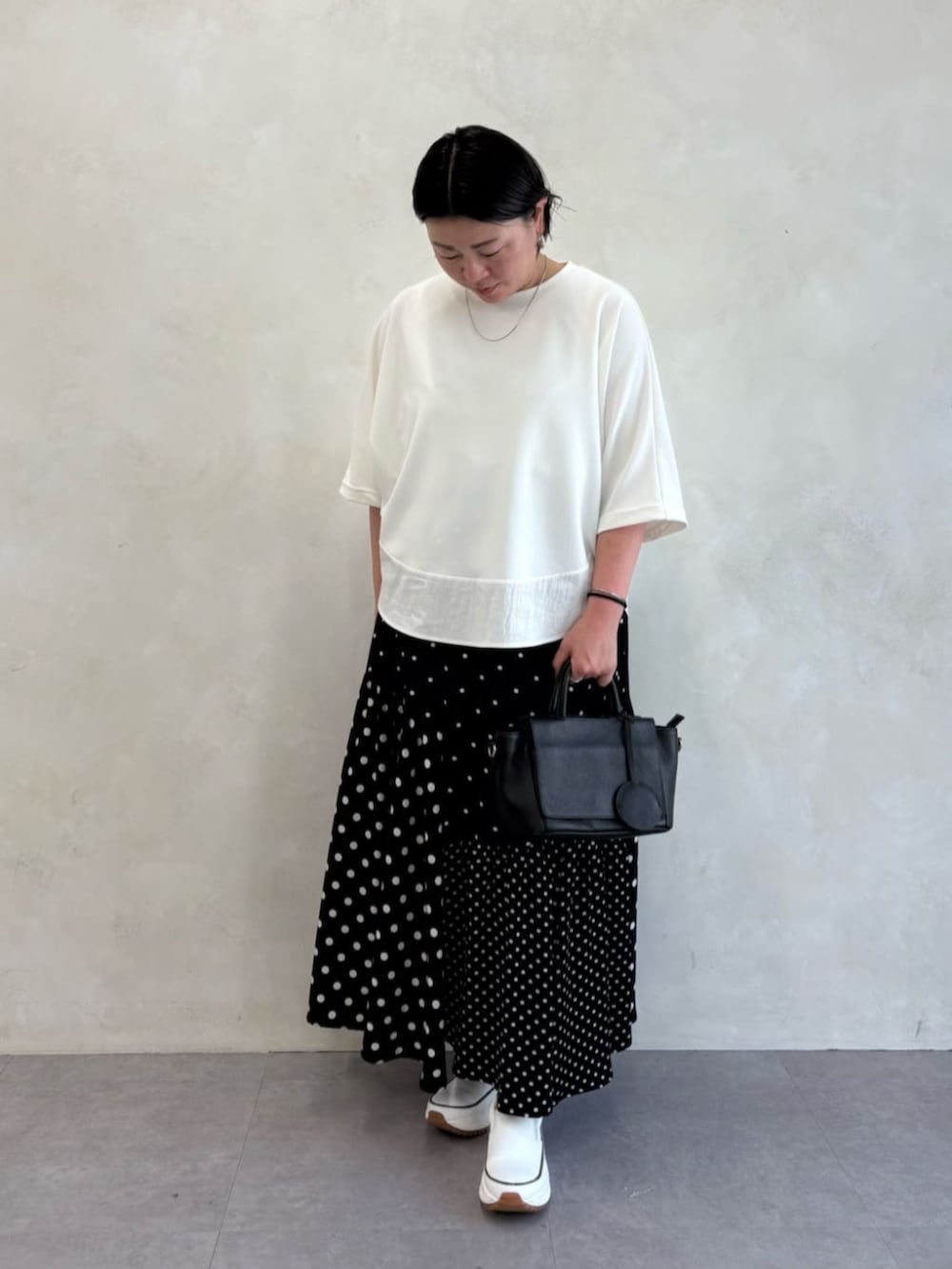 ブラック系のスカート、ホワイト系のTシャツ/カットソー、ホワイト系のスニーカーを着用したレディースの春コーディネートの3枚目の写真