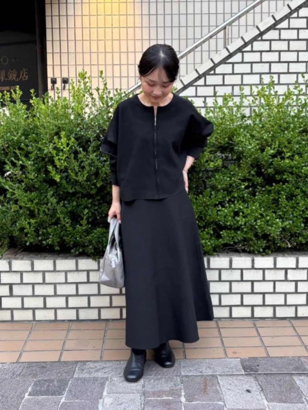 グレー系のボストンバッグ、ブラック系のスカート、ブラック系のカーディガン/ボレロを着用したレディースの秋コーディネートの3枚目の写真