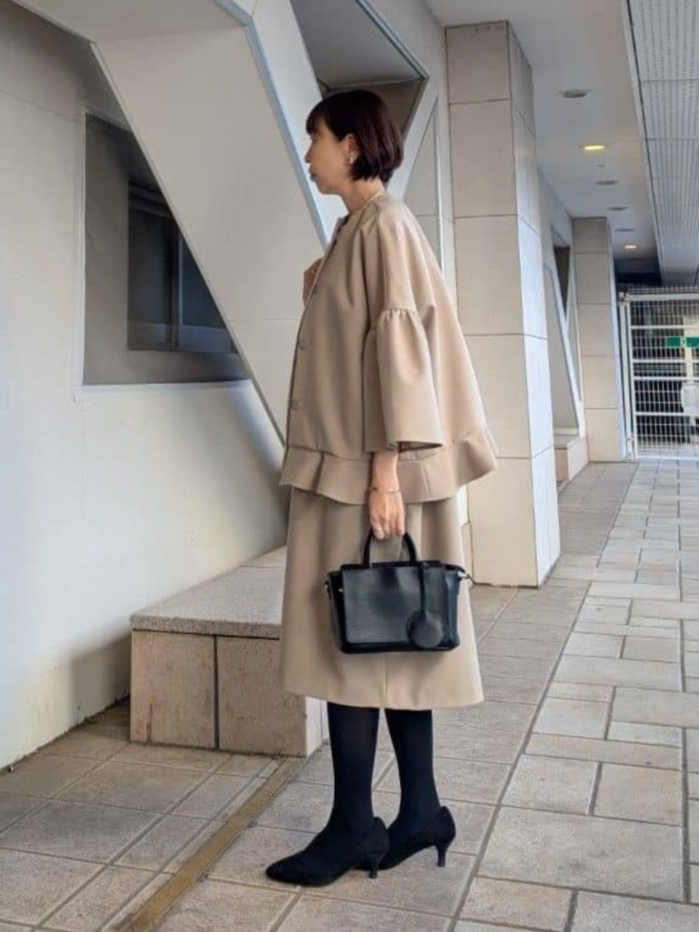 ブラック系のハンドバッグ、ベージュ系のワンピース、ベージュ系のその他アウターを着用したレディースの冬コーディネートの2枚目の写真