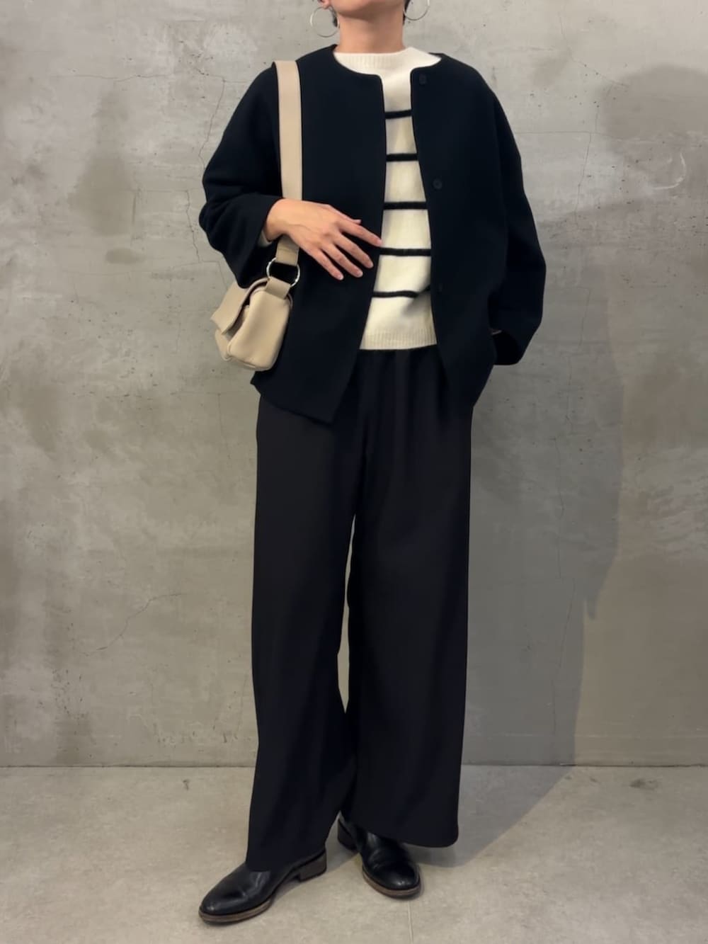 ブラック系のノーカラーコート、ブラック系のその他パンツ、ホワイト系のショルダーバッグを着用したレディースの冬コーディネートの2枚目の写真