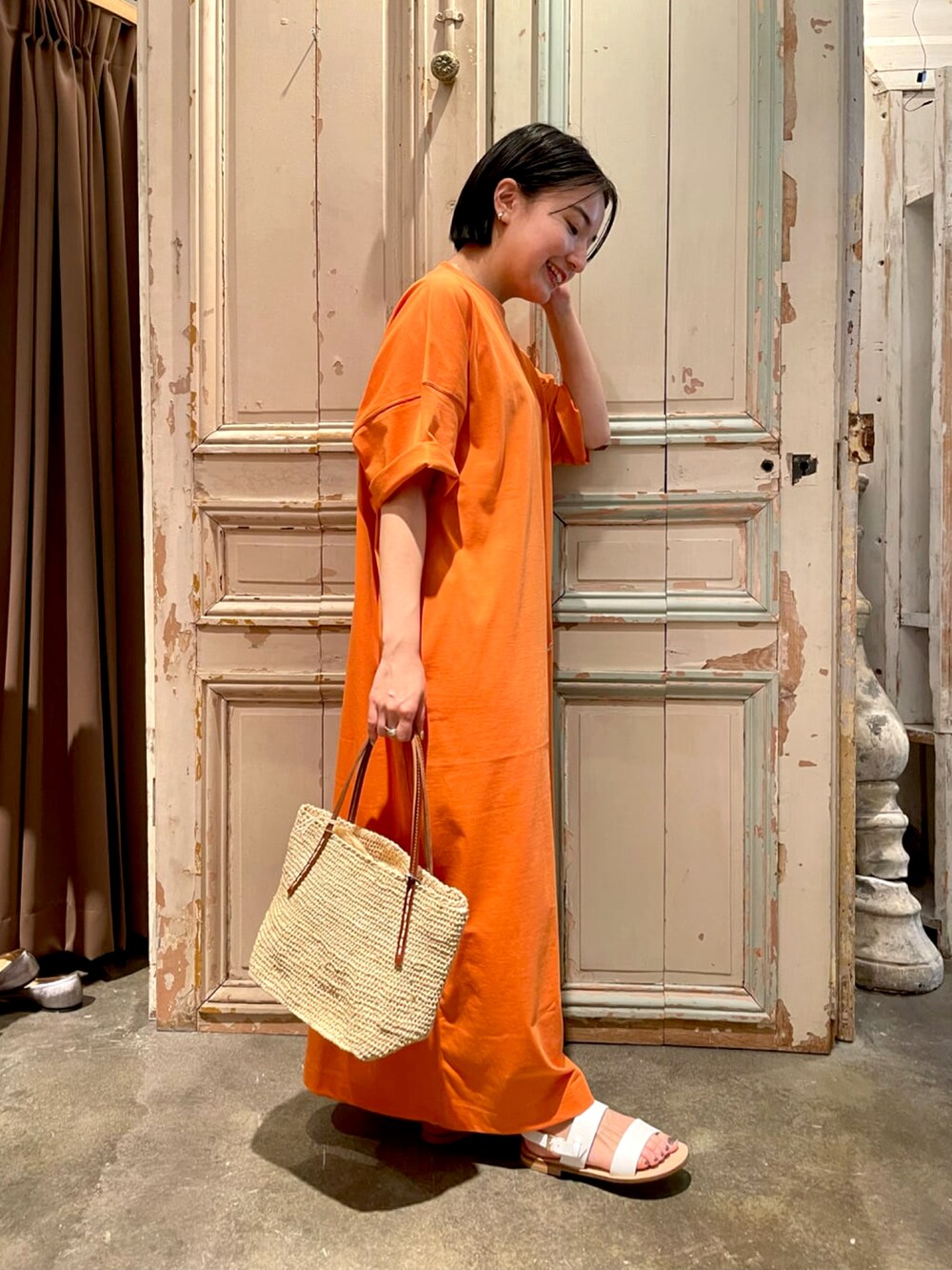 オレンジ系のTシャツ/カットソー、ホワイト系のかごバッグ、ホワイト系のサンダルを着用したレディースの春コーディネートの2枚目の写真