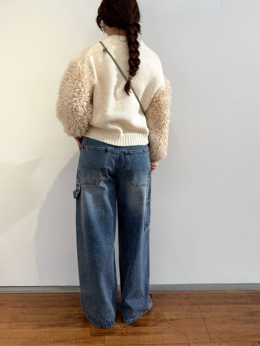 ブルー系のデニムパンツ、ホワイト系のニット/セーター、グリーン系のポーチを着用したレディースの秋コーディネートの4枚目の写真