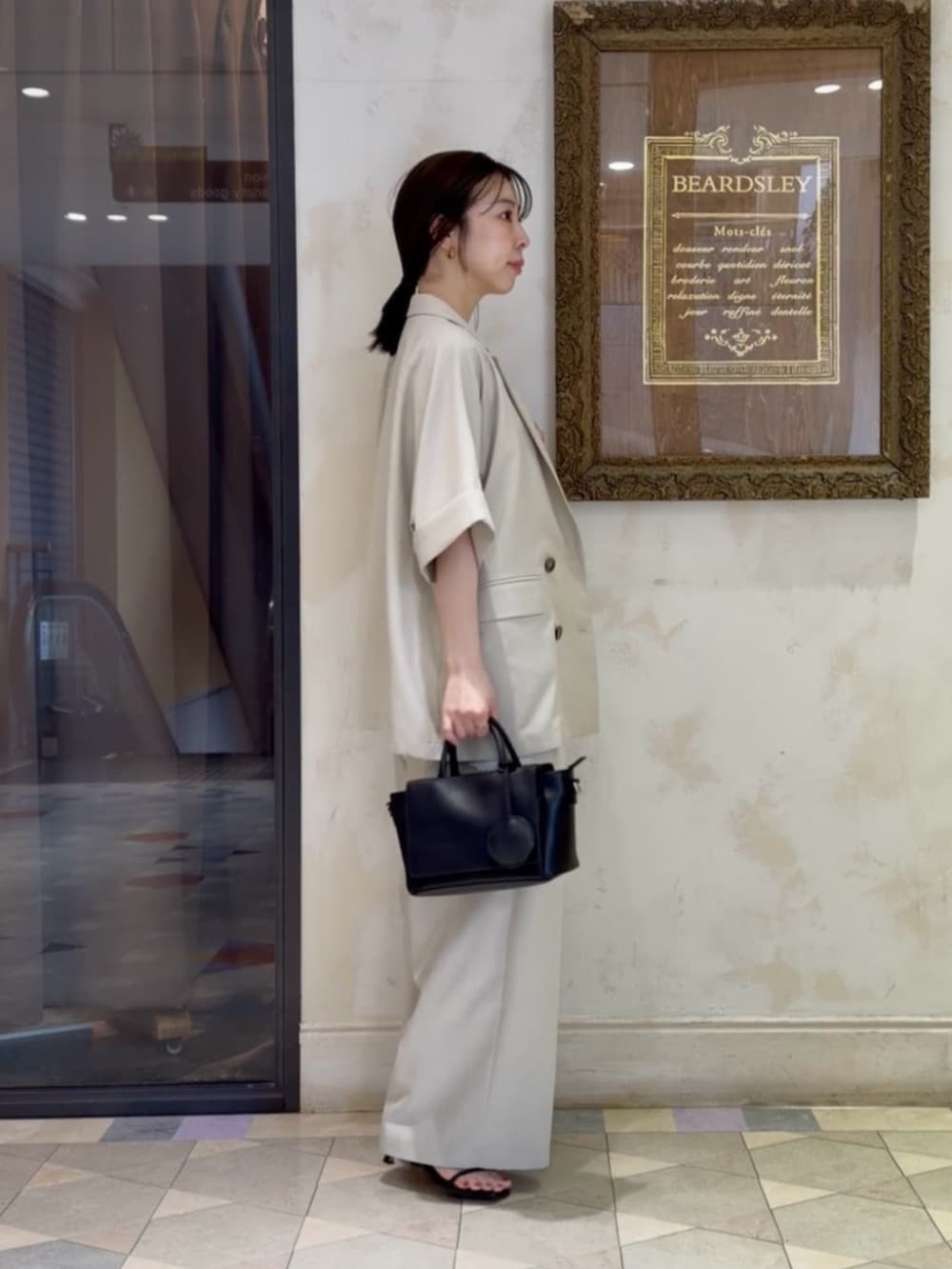ブラック系のハンドバッグ、ベージュ系のテーラードジャケット、ホワイト系のキャミソールを着用したレディースの春コーディネートの2枚目の写真
